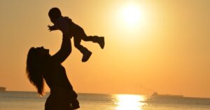 Silhouette of a mother lifting her child at a sunset beach, capturing warmth and love.