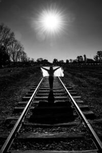 Black and white image of a silhouette on a railroad track under a dramatic sun.
