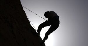 Silhouette of a person rock climbing in Damascus, Syria, against a bright sky.