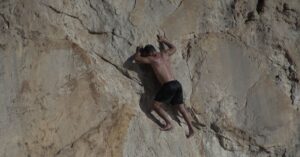 Athletic man engaged in rock climbing on a natural cliff face under sunlight.