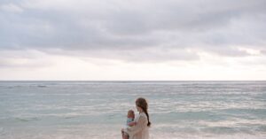 A serene beach scene featuring a mother holding her baby by the ocean during summer.