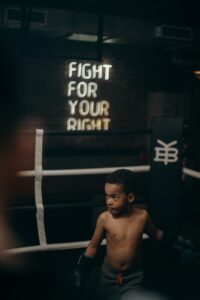 A child boxer stands confidently in a dimly lit boxing ring with motivational text in the background.
